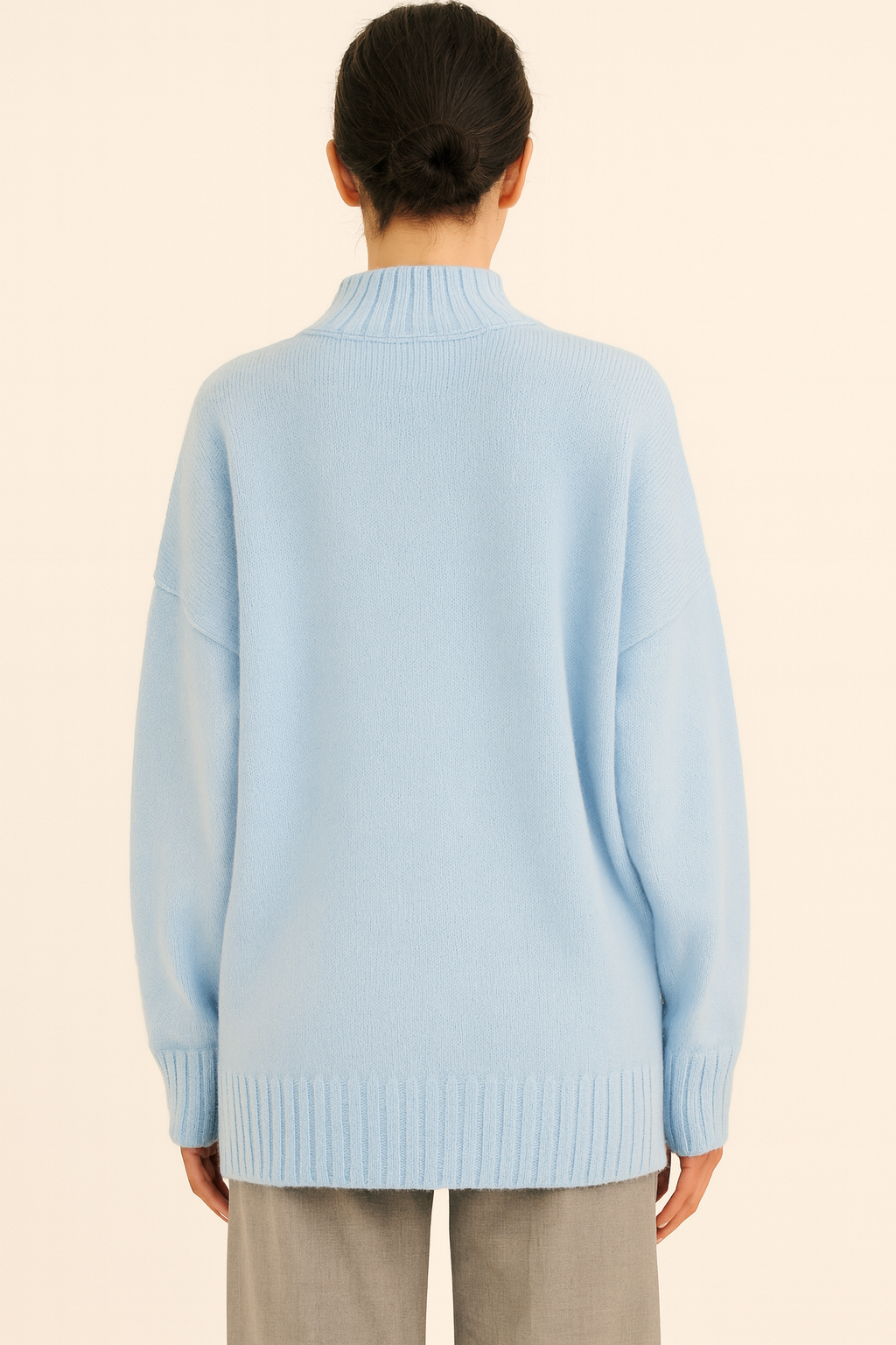 Back view of light blue Nordash Oversized Turtleneck Sweater, oversized knit with dropped shoulders, paired with beige trousers on beige backdrop.