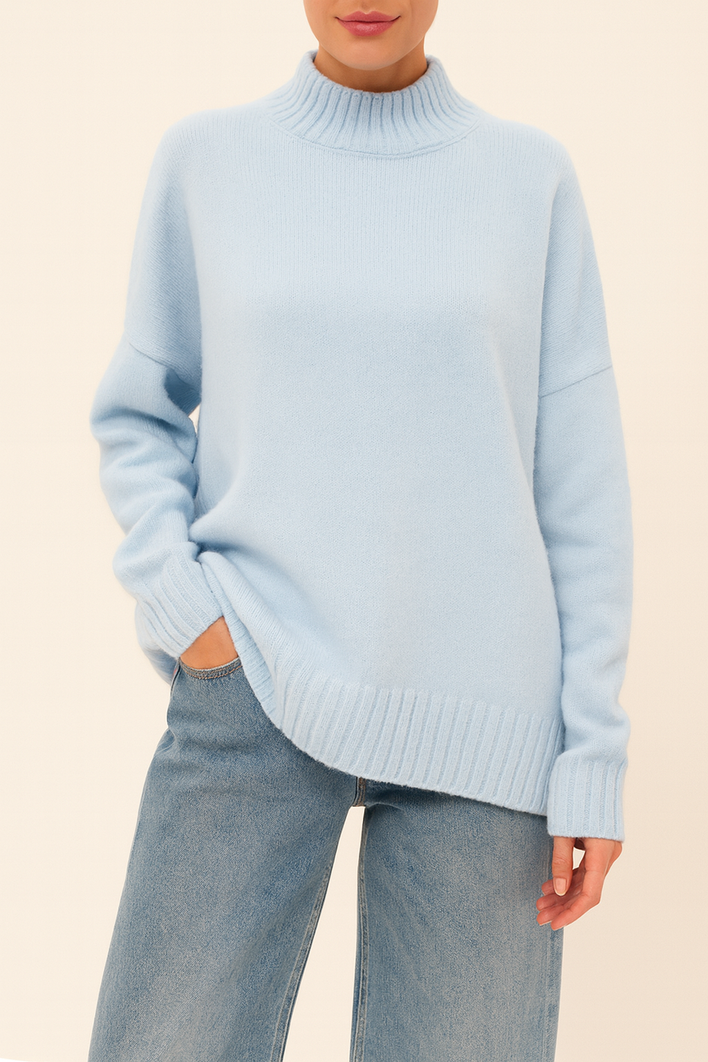 Model wearing Nordash Oversized Turtleneck Sweater in light blue, premium knit with dropped shoulders, paired with denim trousers on beige backdrop.