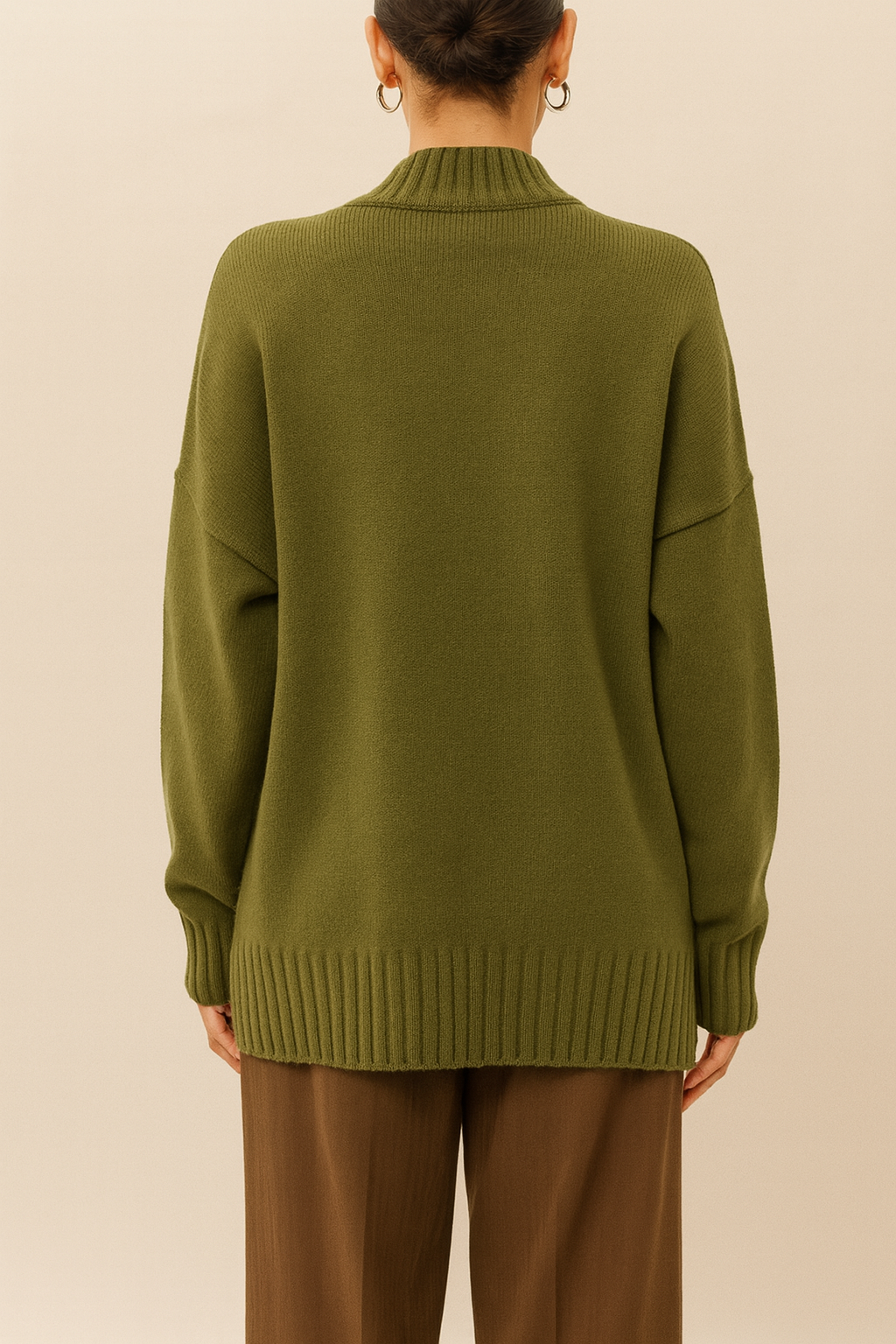 Back view of olive green Nordash Oversized Turtleneck Sweater, relaxed oversized fit, styled with brown tailored trousers against neutral background.