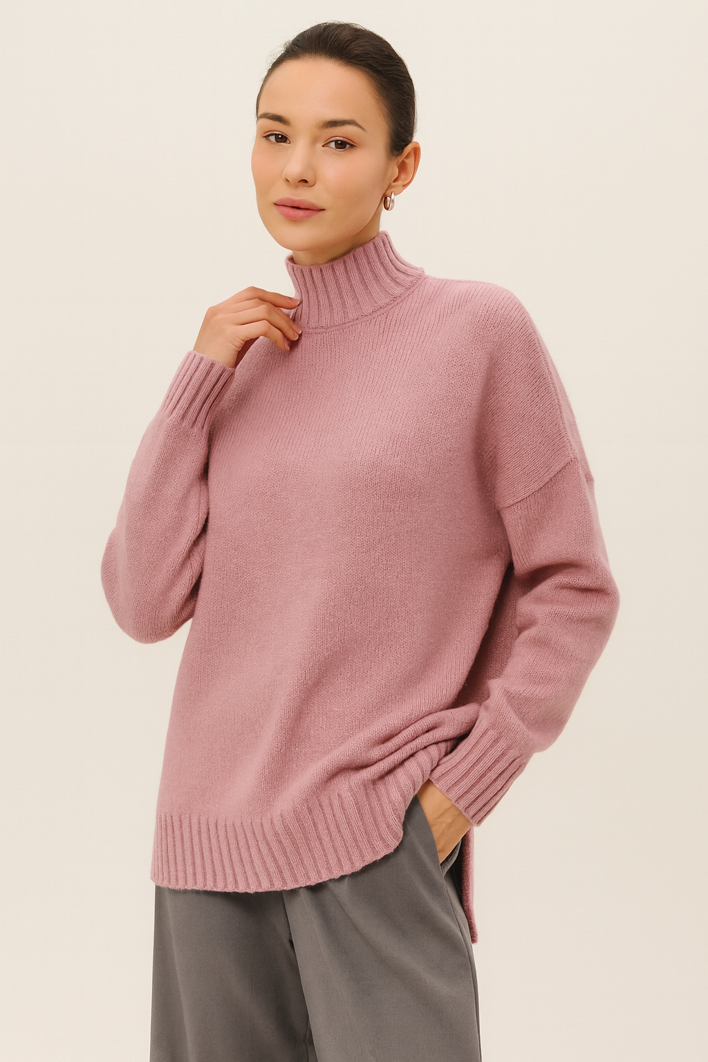 Nordash Oversized Turtleneck Sweater in dusty rose, oversized knit with dropped shoulders, styled with gray trousers in minimalist studio setting.