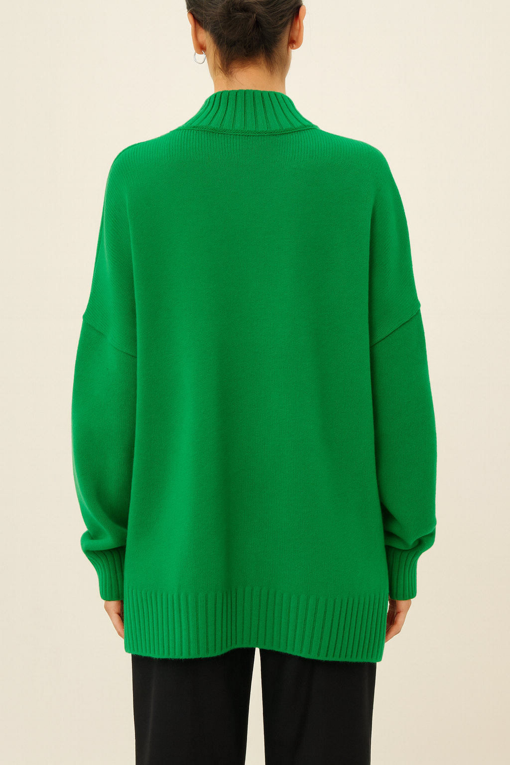 Back view of emerald green Nordash Oversized Turtleneck Sweater, ribbed collar and cuffs, paired with tailored trousers in softly lit studio.