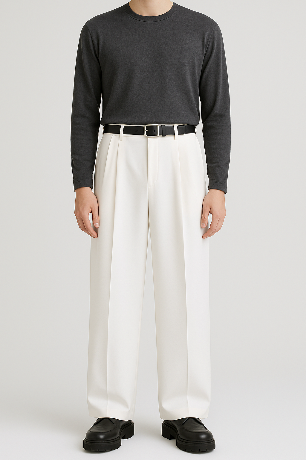 Front view of men’s off-white wide, full-length pleated trousers with deep double pleats and extra-wide straight leg, paired with a tucked-in dark brown crewneck shirt, black leather belt, and black loafers against a seamless light-grey background.