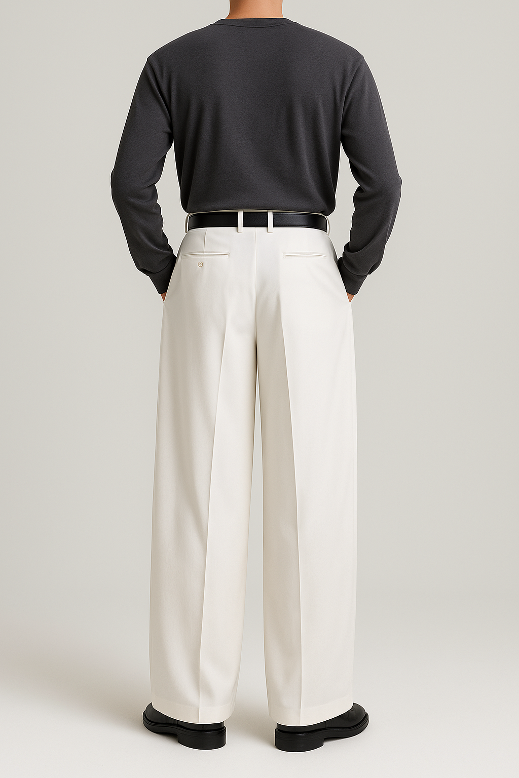 Back view of men’s off-white wide, full-length pleated trousers with mid-rise waistband, back welt pockets, and flowing wide-leg silhouette, styled with a tucked-in dark brown crewneck shirt, black belt, and black loafers.